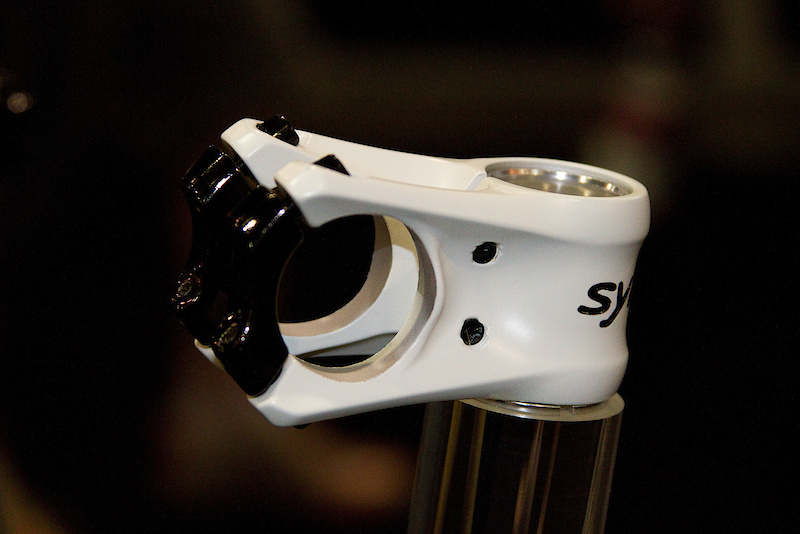 And here I thought that you couldn't possibly reinvent the mountain bike stem... The Syncros FRIC stem is certainly a departure from the norm and can brag about being both impressively light and sporting some unique features. Firstly, this curvy unit is actually forged (although not in the fires of hell), not CNC'd as you might have first guessed. While the fine gentlemen at Syncros were not about to share how the shape comes to life via the forging, it is unusual to see a piece as shapely as the FRIC use this process for manufacturing. I'm not about to go on a big spiel as to why forging can create stronger parts, that is for you to look up, but it is a common method of producing a light and strong final product. The stem's FRIC name is an acronym for FreeRide Intelligent Clamp and refers to the faceplate bar clamp that runs a full 260 degrees around the handlebar. While the forging process contributes to the stem's light 124 gram weight, the extra bar clamp grip area also plays a part in allowing for a lighter weight due to not as much material being needed. Although mega light, the FRIC is designed for full on heavy duty use as the name suggests. After being shown the stem I immediately assumed that your handlebar controls would have to be removed from one side during the installation, but this isn't the case. The 260 degree clamp leaves enough room for you to fit the tapered part of your bar through, not the 31.8 clamping area. Listen to the audio below to learn more!